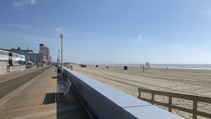 A wooden boardwalk with benches and trash bins, leading to a sandy beach with a clear sky. - Available Country Calling! Linens and parking. Short walk to Beach and Boards. (Ocean City)