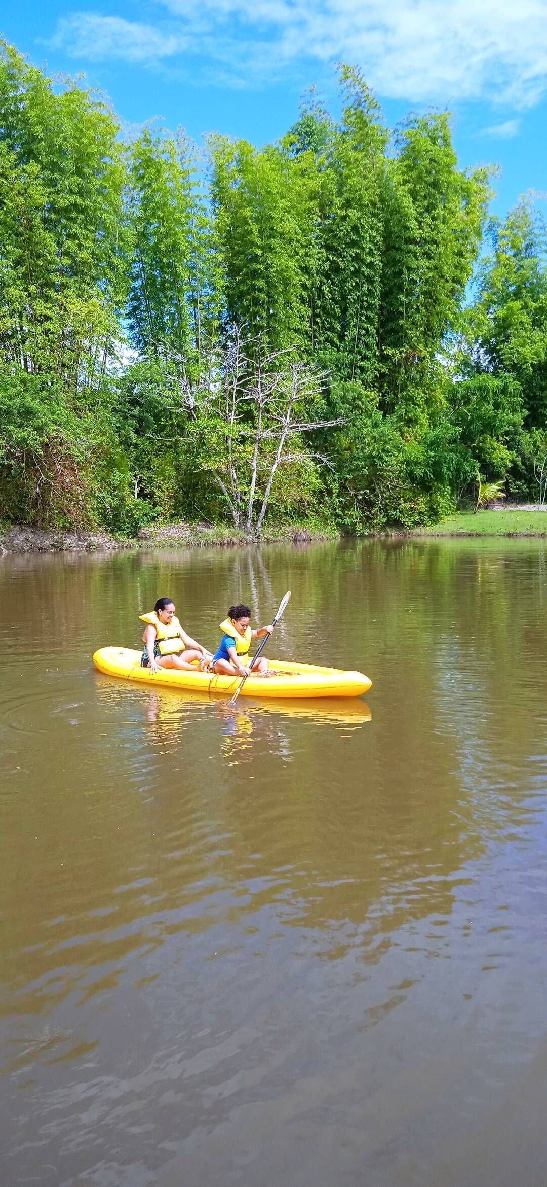 Two people in a yellow raft on a calm river surrounded by lush greenery.