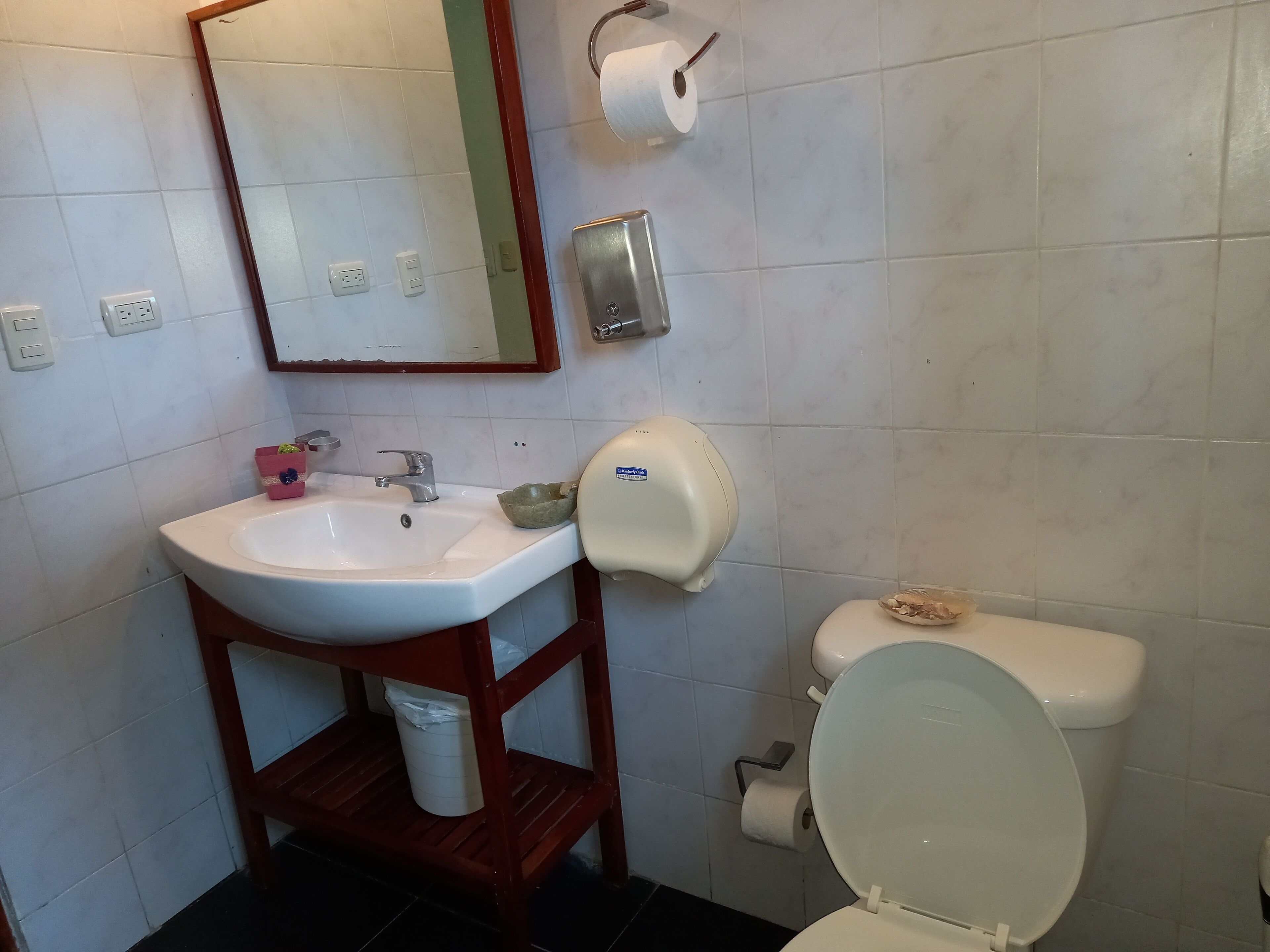 Un baño con un lavamanos blanco, un espejo, un inodoro y un dispensador de toallas de papel.