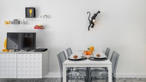 Ett modernt matområde med ett vitt bord, genomskinliga stolar och ett vitt skåp med en tv.