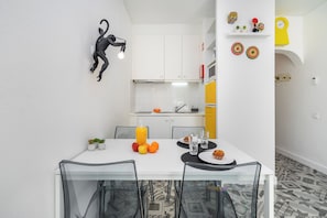 A compact kitchen with white cabinets, a small dining table with chairs, and a fruit bowl.