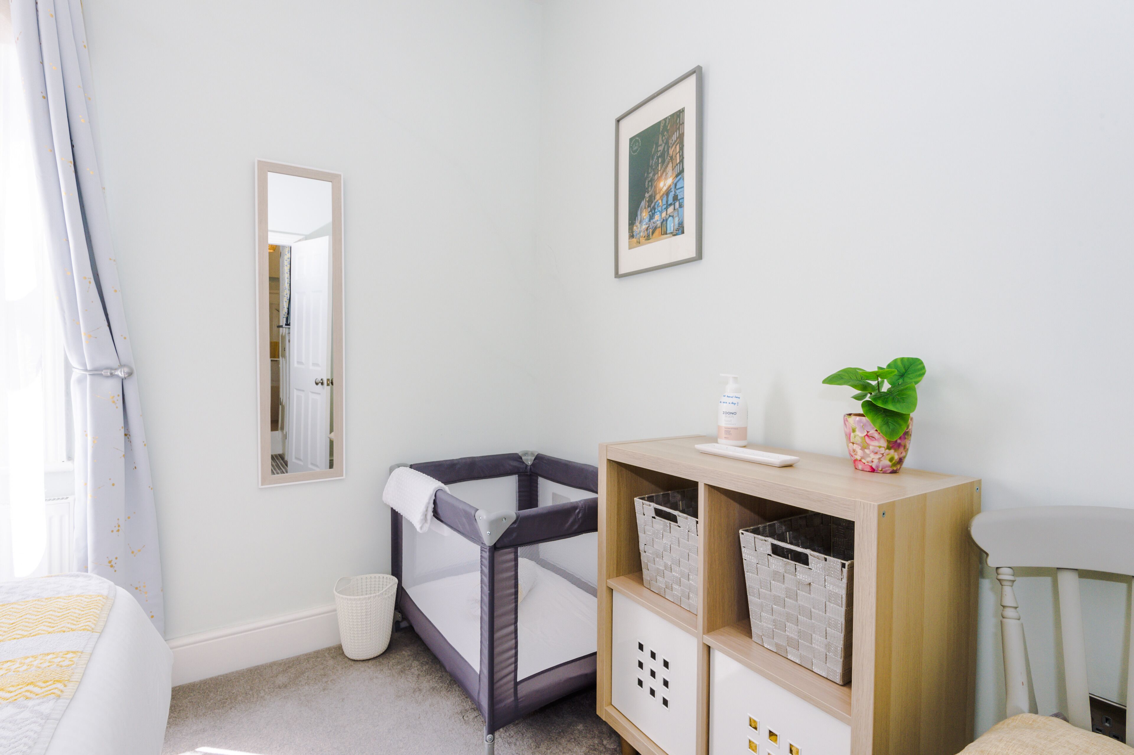 Una habitación infantil con una cuna, un cambiador, un estante con cestas, un espejo y un cuadro en la pared.