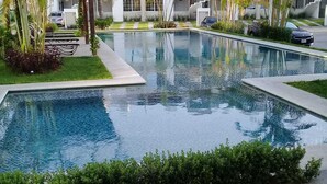 Un hôtel moderne doté d’une piscine rectangulaire, entourée d’une végétation luxuriante et de palmiers.