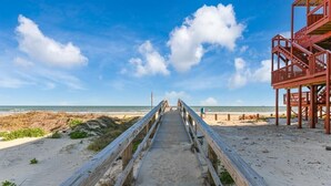 En träpromenad som leder till en strand med ett badvakts torn.