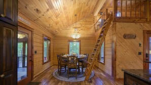 Ein Holzblockhaus-Innenraum mit Esstisch, Stühlen, einer Kandelaber und einer Treppe.