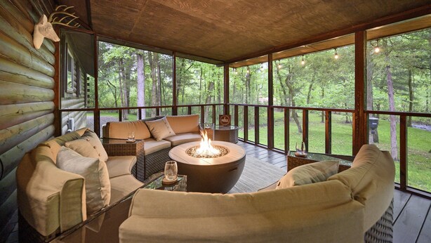 Ein gemütlicher Sitzbereich im Freien mit Feuerstelle, Holzterrasse und Blick auf den Wald.