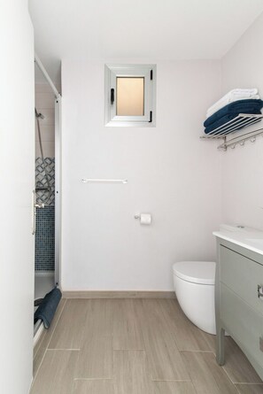 A modern bathroom with a toilet, a small window, a towel rack, and a shower area.