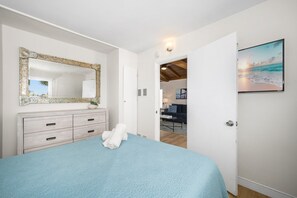 Une chambre à coucher avec un grand lit, une commode, un miroir et une porte donnant sur un espace de vie comprenant un canapé et un tableau.