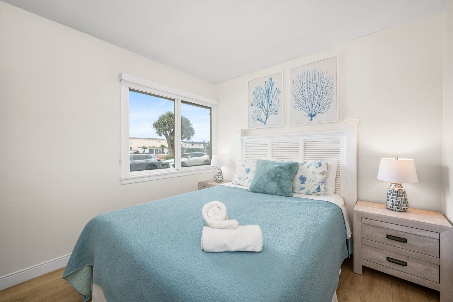 A bedroom with a large bed, a nightstand with a lamp, and a window with a view of the outside.