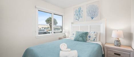 A bedroom with a large bed, a nightstand with a lamp, and a window with a view of the outside.