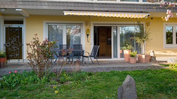 A two-story building with a yellow facade, large windows, and a covered patio area with outdoor furniture. - Apartment Oasis - Gemütliche Wohnung mit Garten (Mendig)
