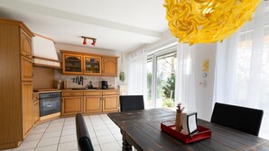 A modern kitchen with wooden cabinets, a black stove, and a dining table with chairs. - Apartment Oasis - Gemütliche Wohnung mit Garten (Mendig)