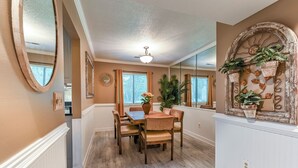 A dining area with a wooden table and chairs, a ceiling fan, and a decorative wall with plants. - Exquisite Summerville Retreat-Walk to Downtown, Festivals & Southern Hospitality (Summerville)