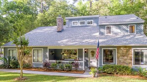 A two-story house with a stone chimney, a front porch with a white picket fence, and an American flag. - Exquisite Summerville Retreat-Walk to Downtown, Festivals & Southern Hospitality (Summerville)
