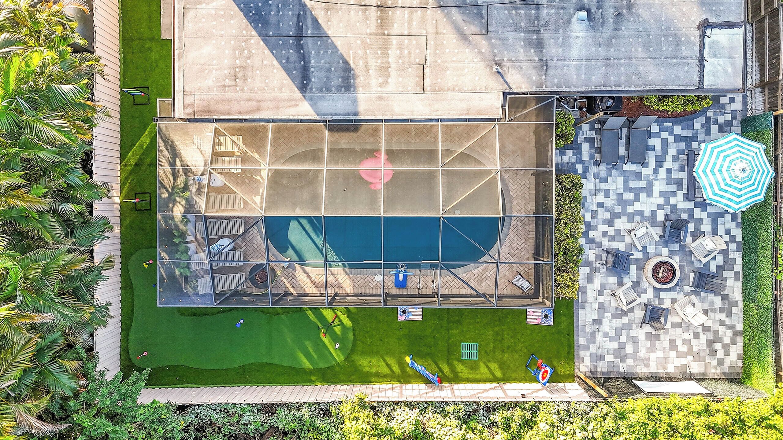An aerial view of a pool area with a surrounding deck, a small garden, and a patio with seating.