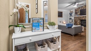 A living room with a white console table, a grey sofa, a fireplace, and a ceiling fan. - Paradise Oasis Heated Pool+Hot Tub+Games & Arcade (Largo)