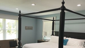 Una cama con dosel de madera oscura, ropa de cama blanca y una mesita de noche con lámpara.