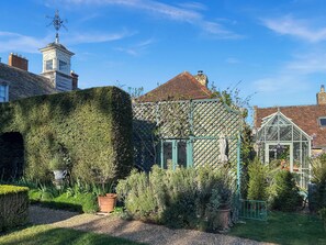 Ein Garten mit Gewächshaus, Hecke und einem Gebäude mit einem Turm.