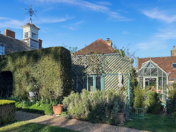 A garden with a greenhouse, a hedge, and a building with a tower.