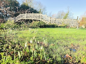 Eine Holzbrücke über ein grasbewachsenes Feld mit Bäumen im Hintergrund.