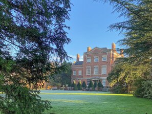 A large brick building with a symmetrical facade, multiple windows, and a well-maintained lawn with outdoor furniture. - 1 bedroom accommodation in Godmanchester (Godmanchester)