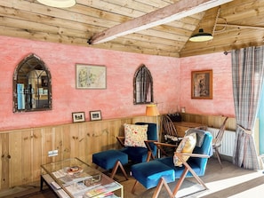 Ein Zimmer mit Holzwandverkleidung, einem Glastisch mit Zeitschriften, einem blauen Sessel und einem Holzstuhl.
