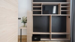 Een moderne kamer met een ingebouwde televisie, houten planken en een klein bureau met een vaas bloemen.