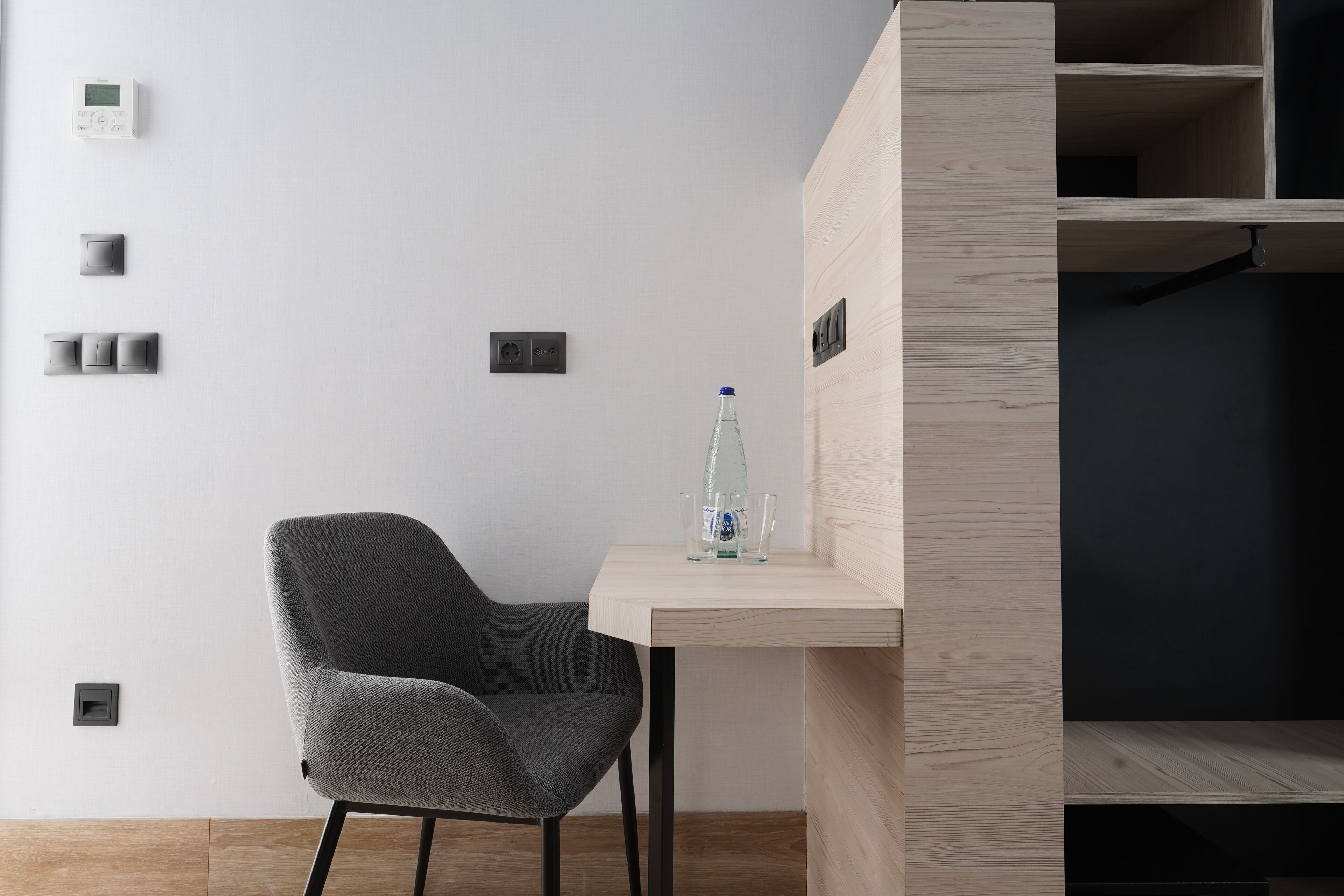 A modern room with a grey chair, a wooden desk, and a water bottle.