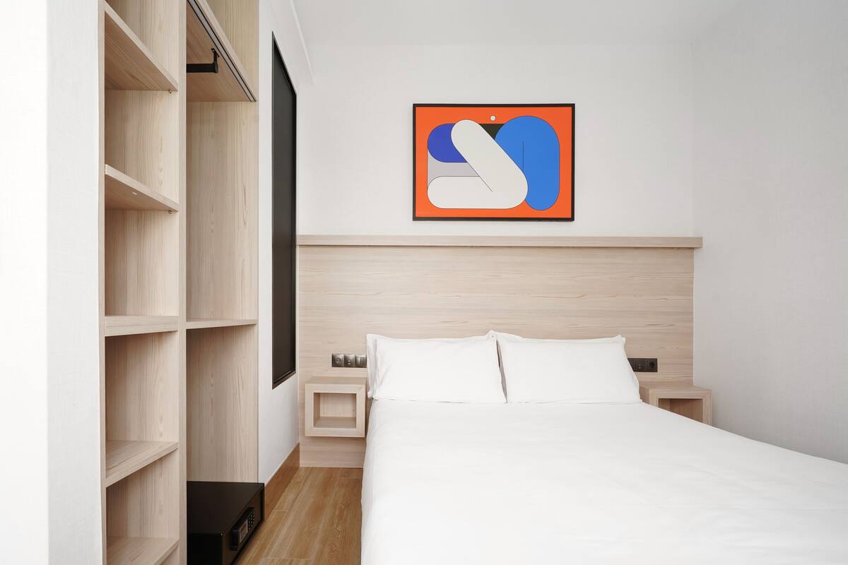 Een moderne slaapkamer met een bed, houten planken, een flatscreen televisie en een abstract kunstwerk in een lijst aan de muur.