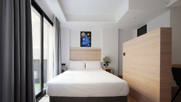 Een moderne slaapkamer met een groot bed, een houten hoofdbord, een nachtkastje met een vaas en een schilderij aan de muur.