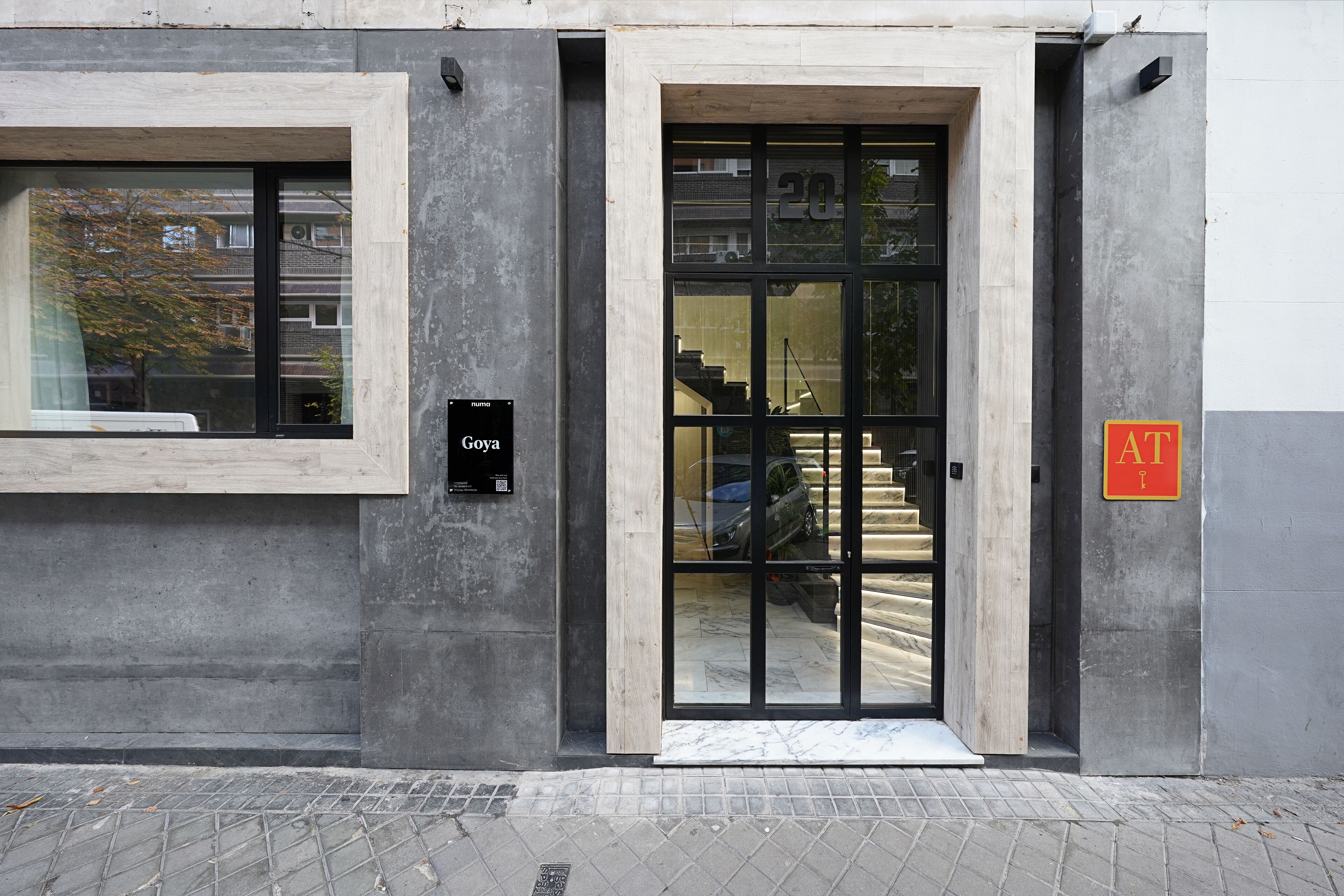 Entrada de un edificio con puerta de cristal, un letrero que dice "Gova" y un cartel rojo con la letra "AT" a la derecha.