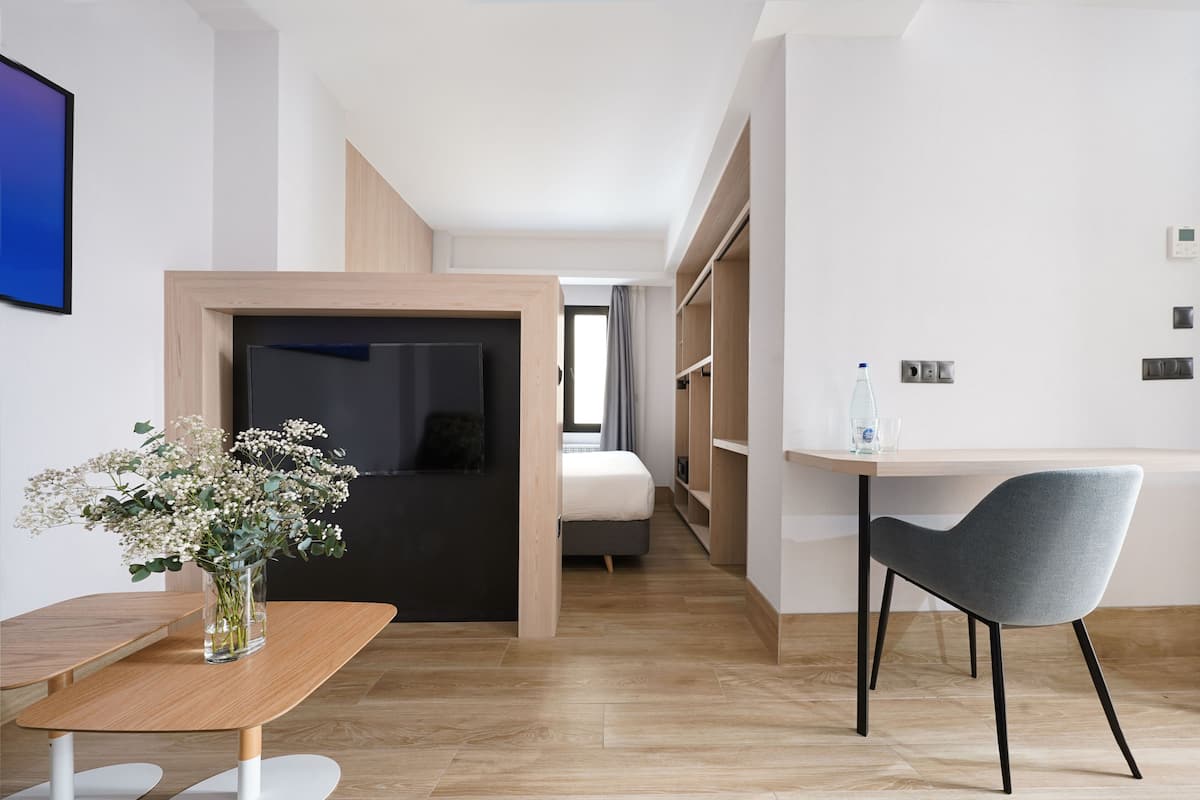 Een moderne hotelkamer met een houten vloer, een zithoek met een tafel en stoelen, een bed en een badkamer die door een open deur zichtbaar is.