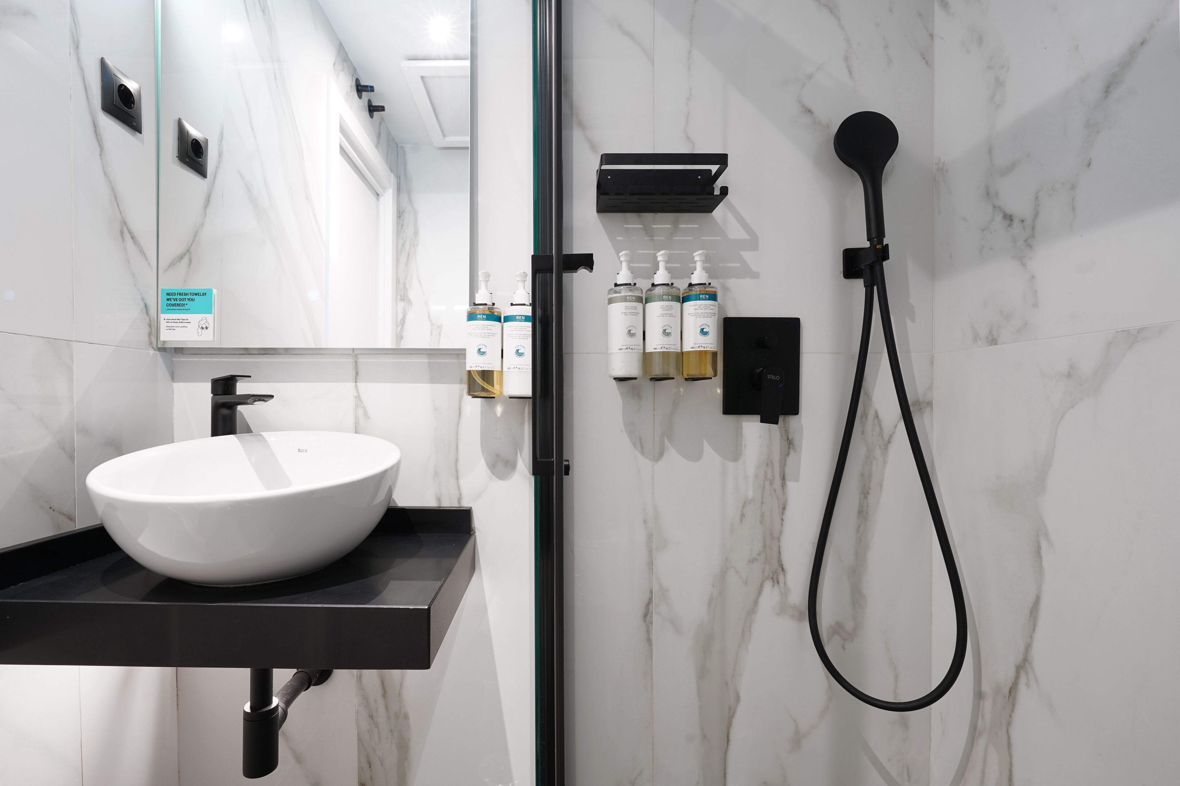 A modern bathroom with a white marble sink, black countertop, and a handheld showerhead.