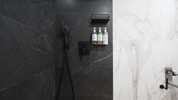 A modern bathroom with a black marble shower, a handheld showerhead, and two bottles of shampoo and conditioner on a shelf.
