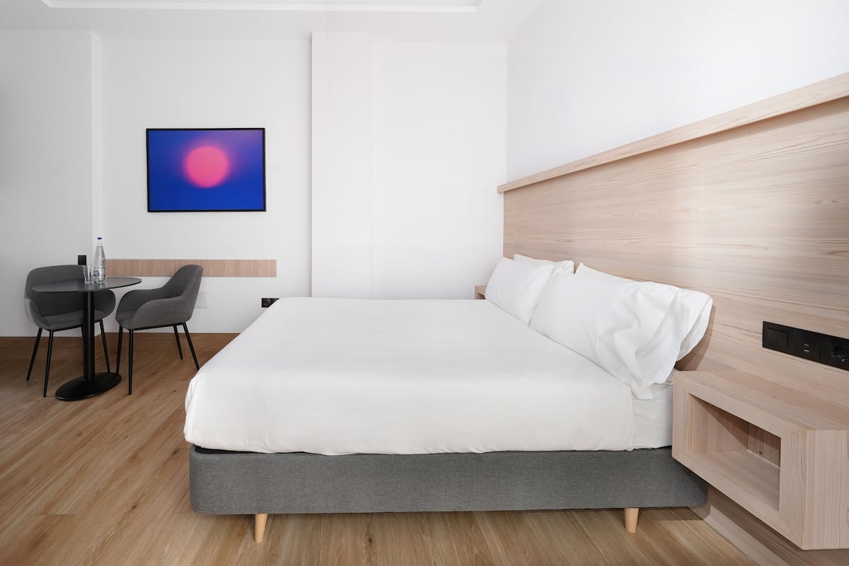 Een moderne hotelkamer met een groot bed, een klein bureau met twee stoelen, een tv aan de muur en een houten hoofdbord.