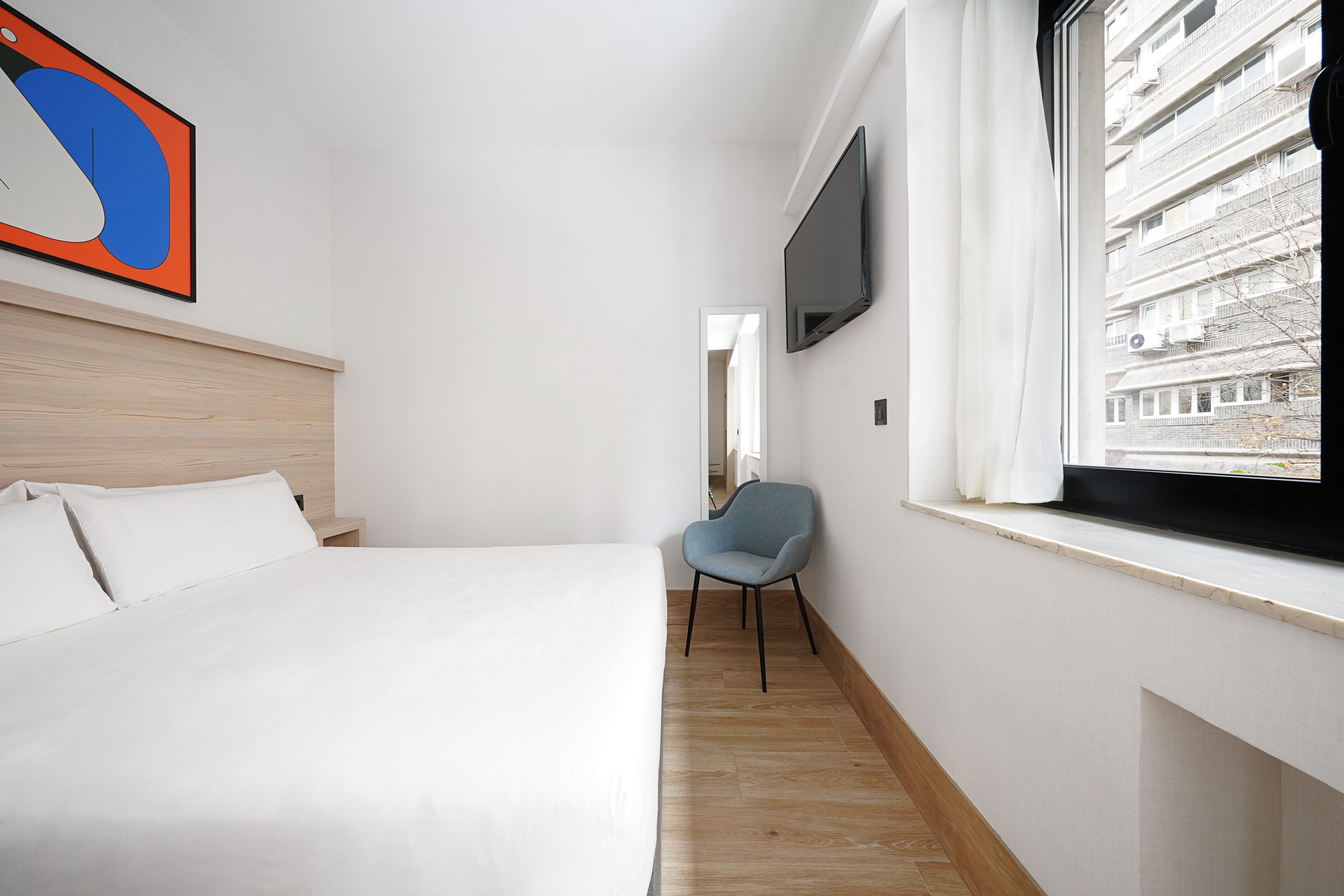Een hotelkamer met een bed, een stoel, een televisie en een raam met uitzicht op gebouwen.