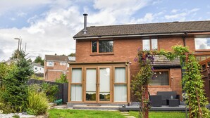 Une maison à deux étages, construite en briques, avec une grande porte d’entrée en verre, une cheminée et un jardin agrémenté d’un patio.