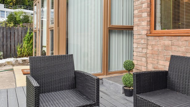 Un bâtiment moderne doté de grandes portes et fenêtres en verre, de meubles en osier pour l’extérieur et d’une petite plante en pot.