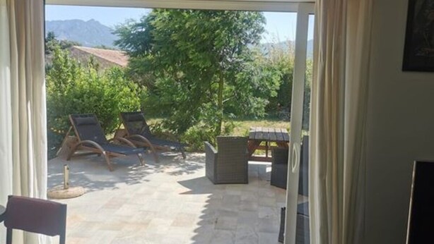 Una habitación con puerta de vidrio corrediza que da a un patio exterior con sillones de descanso y una pérgola.