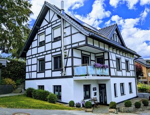 A two-story house with a balcony, a chimney, and a well-maintained garden. - Ferienwohnung Hermes - Eicherscheid (Simmerath)