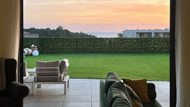 Una sala de estar moderna con un amplio ventanal corredizo que da a un césped cuidado y una vista al atardecer.