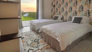 Un dormitorio con dos camas, un ventanal grande y un papel tapiz estampado.