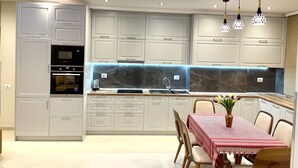 Une cuisine moderne avec des armoires blanches, un four encastré et un coin repas avec une table dressée pour quatre personnes.