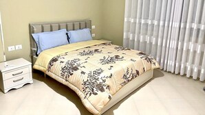 Une chambre à coucher avec un lit, une table de chevet, une lampe et une fenêtre avec des rideaux.