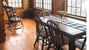 L’intérieur d  ’un chalet en bois comprend une table à manger, des chaises, des fauteuils à bascule et de grandes fenêtres.