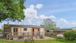 A rustic cabin with a wooden deck, a picnic table, and a large tank in the yard.
