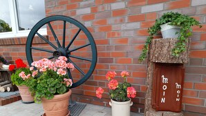 A brick wall with a large wheel, potted plants, and a wooden structure with the word "MOON" on it. - Vacation apartment in a quiet, rural location (Großefehn)