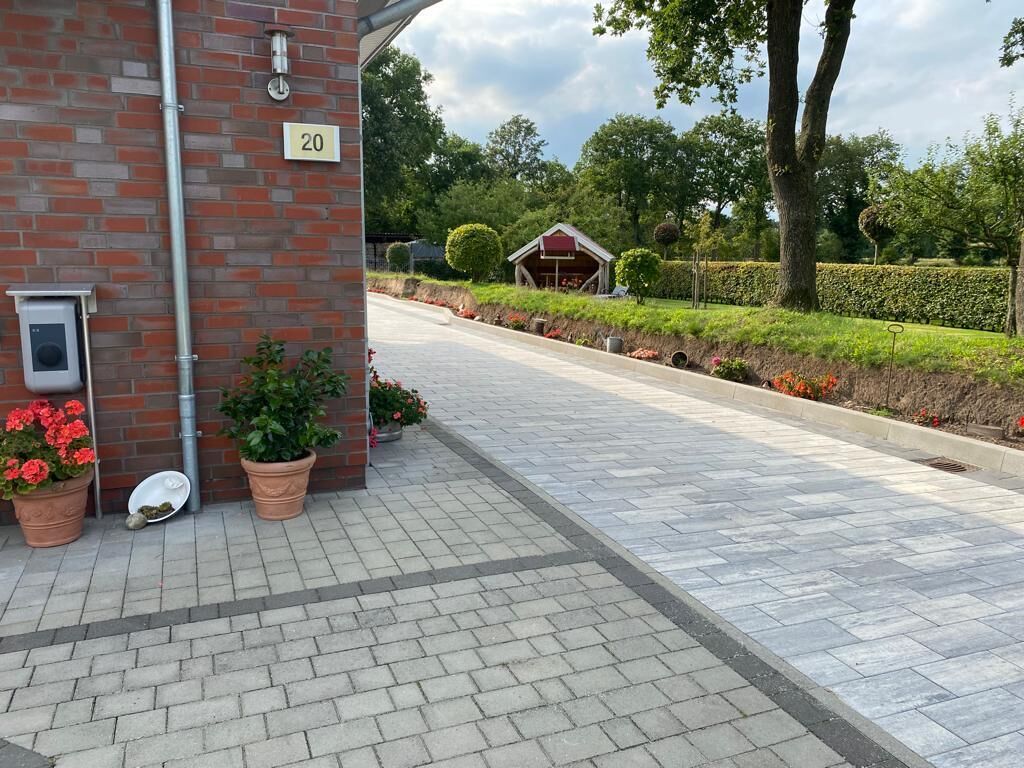 A paved walkway with potted plants and a brick building with a number sign.