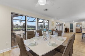 Uma sala de jantar com uma mesa grande posta para seis pessoas, janelas amplas e vista para o exterior.