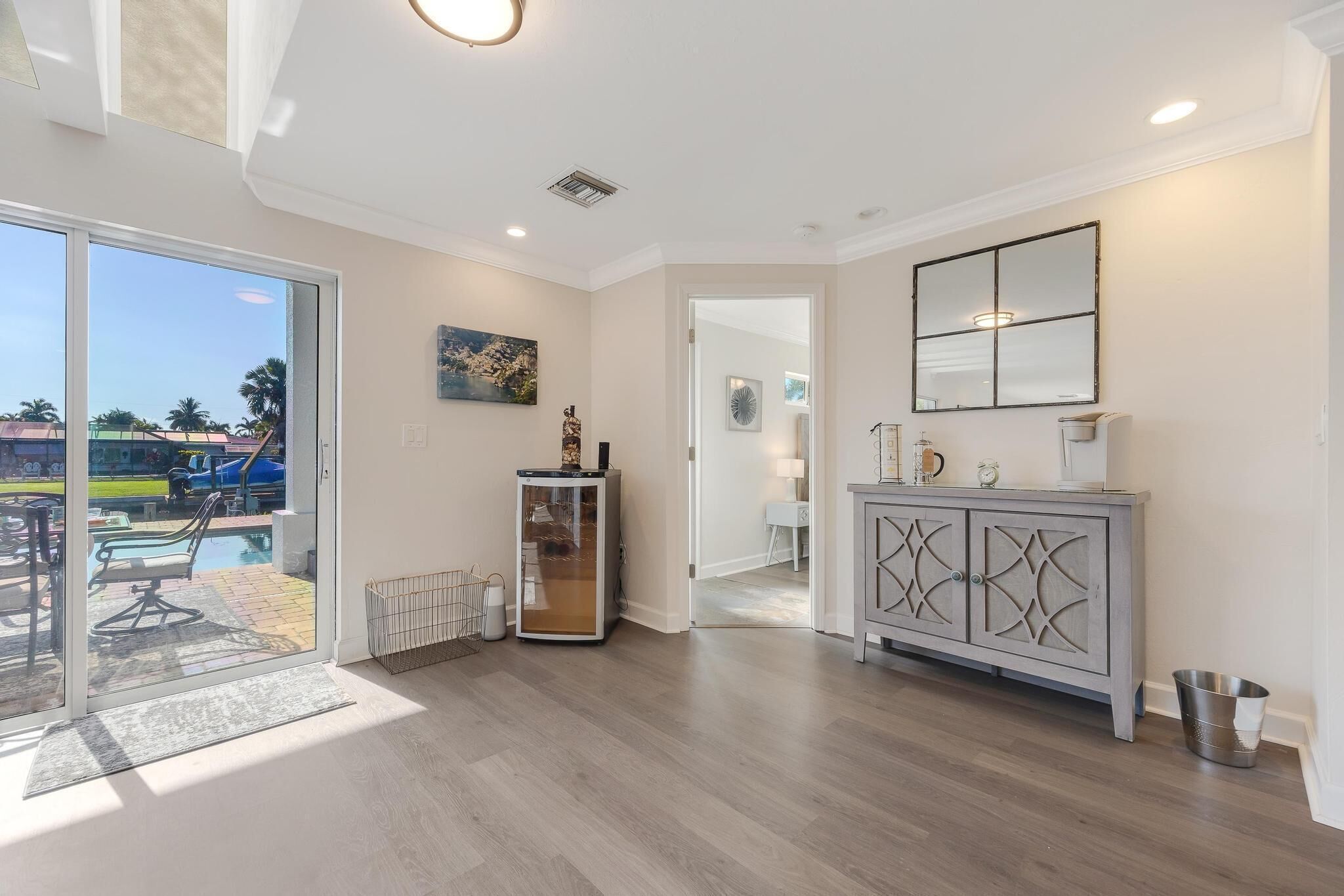 A spacious room with a large sliding glass door leading to a pool area, a grey cabinet with decorative cutouts, and a ceiling with recessed lighting.
